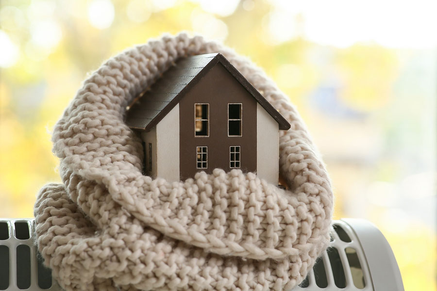 Une maison miniature enroulée dans une écharpe en crochet.